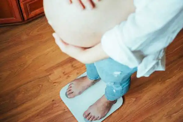 Image of woman weighing herself and experiencing weight gain through pregnancy Newcastle under Lyme